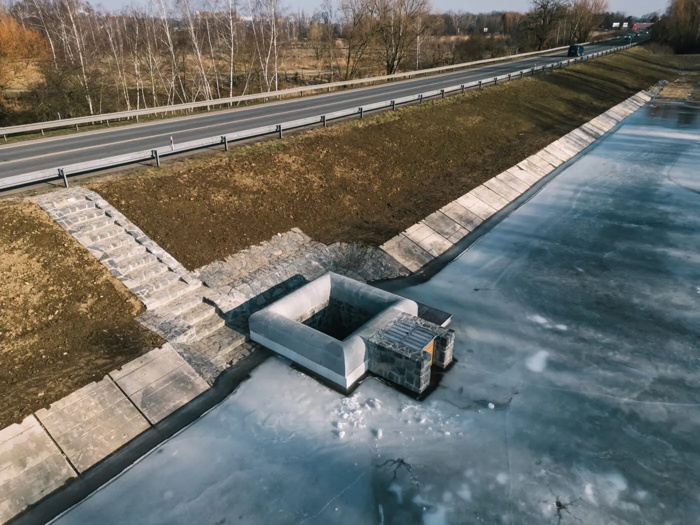 Původní vypouštěcí zařízení s bezpečnostním přelivem jsme odstranili a nahradili je novým sdruženým železobetonovým objektem, který je obložen kamenem a vede k němu nově obslužná cesta.